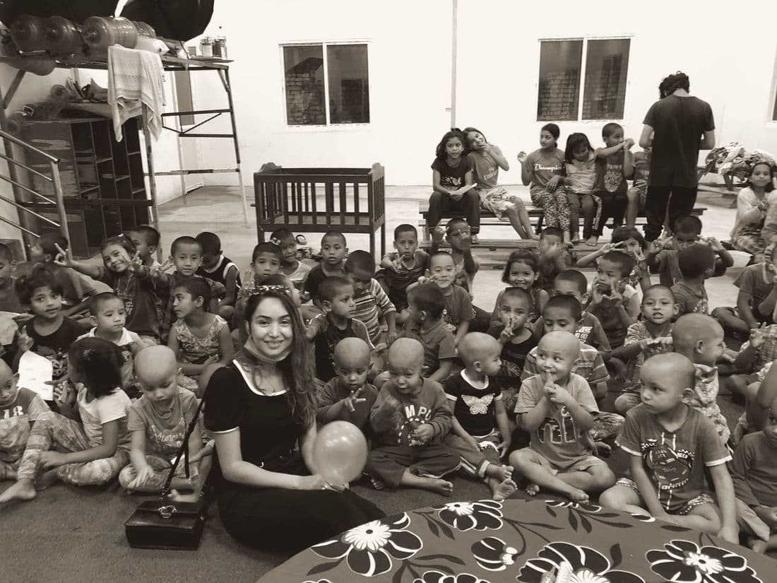 Pooja sitting among a large group of children in a hall