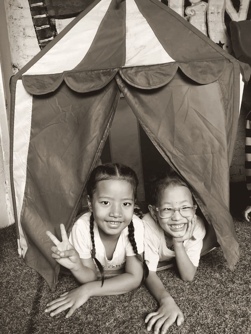 Two girls grinning from inside a play tent