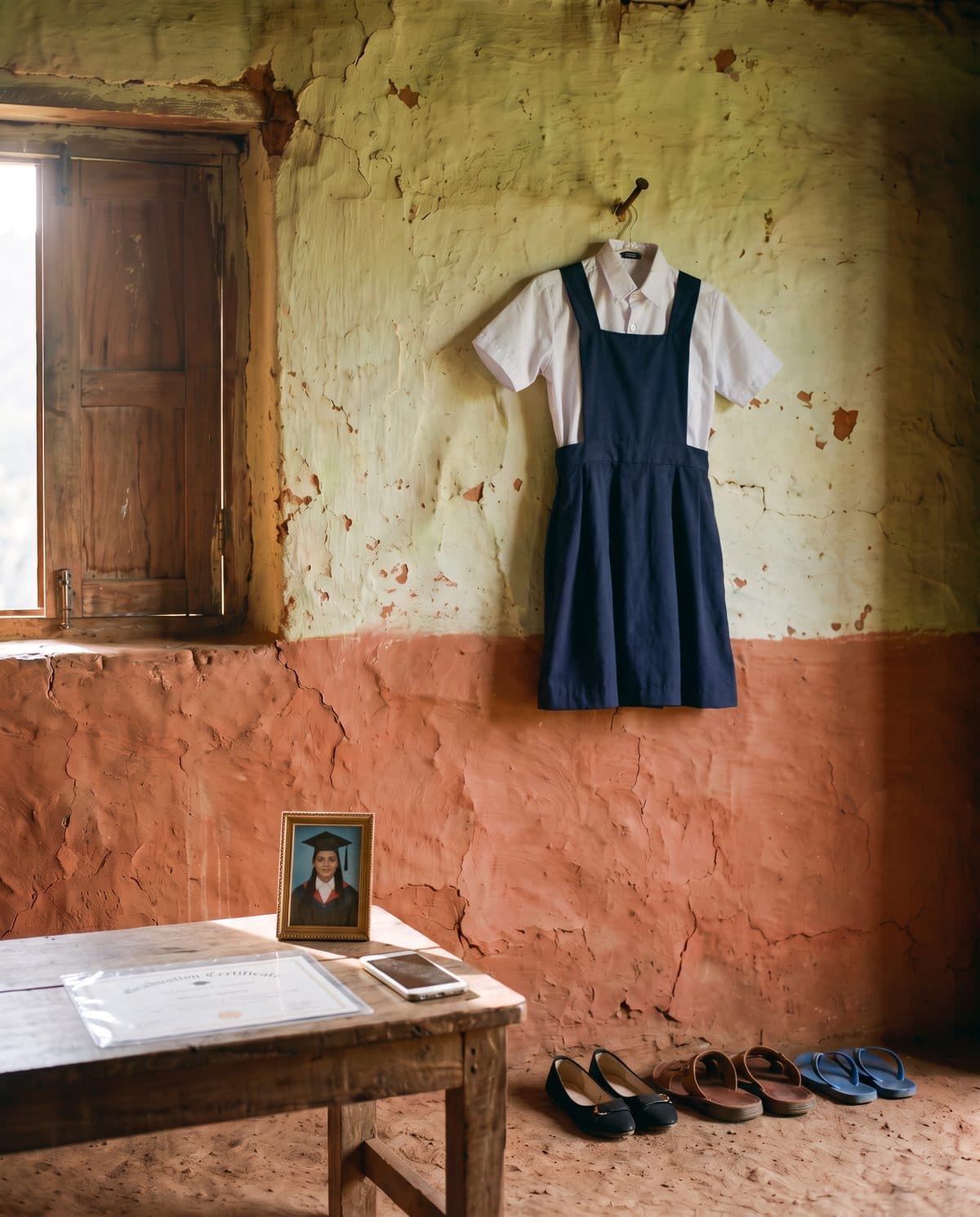 A new small school uniform on the nail for a younger child, her graduation certificate on the table